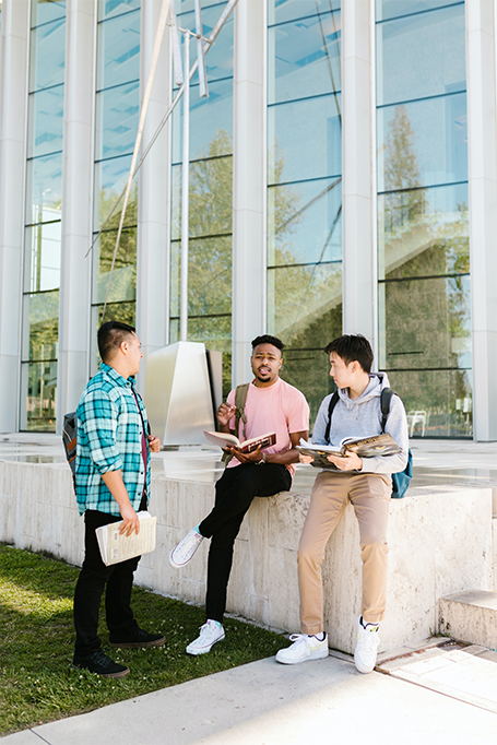 three male students talking outside of a building